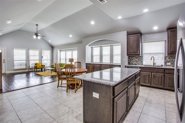 kitchen featuring lofted ceiling, sink, light stone counters, light tile patterned floors, and a kitchen island