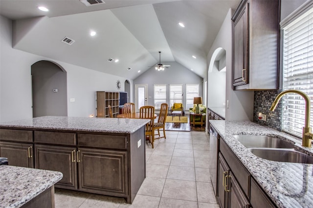 kitchen with light stone counters, a center island, sink, and dark brown cabinets