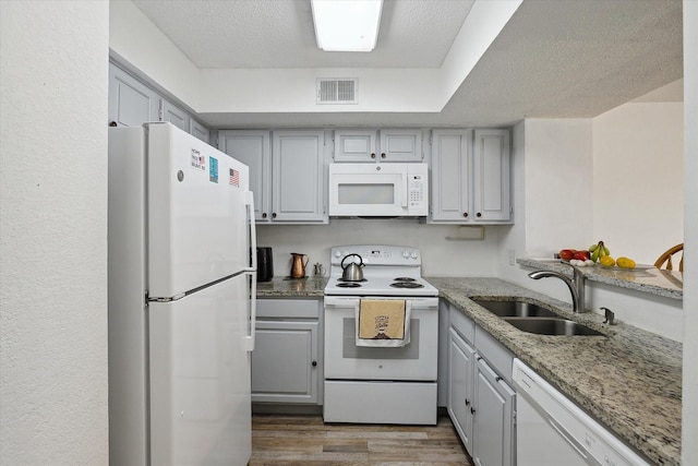 kitchen with a sink, visible vents, white appliances, and gray cabinetry