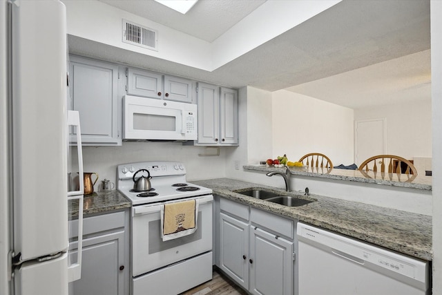 kitchen with white appliances, light stone counters, visible vents, a sink, and light wood-style floors