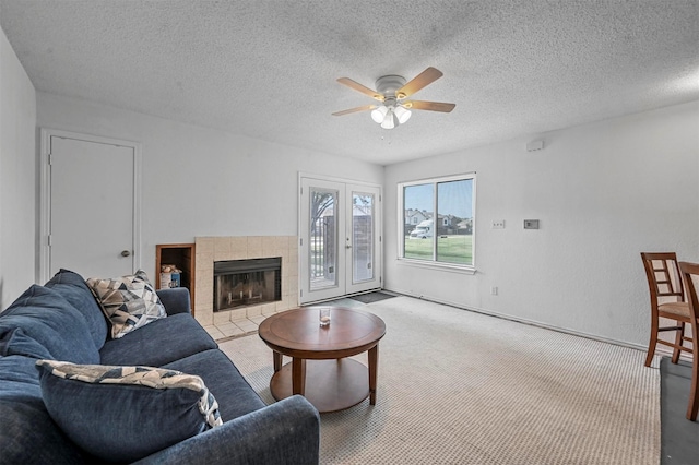 carpeted living room featuring a textured ceiling, a tile fireplace, french doors, and ceiling fan