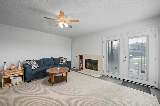 living room featuring a tile fireplace, ceiling fan, carpet floors, a textured ceiling, and french doors