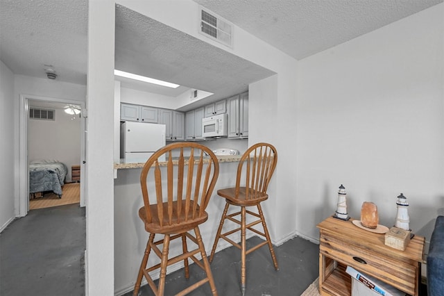 kitchen featuring white appliances, a textured ceiling, a breakfast bar area, and gray cabinetry