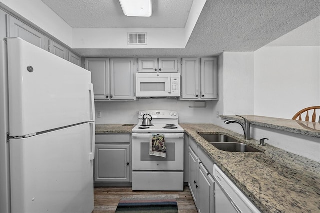 kitchen with sink, white appliances, gray cabinets, dark hardwood / wood-style floors, and light stone countertops