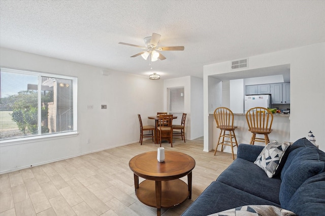 living area with light wood-type flooring, a textured ceiling, visible vents, and a ceiling fan