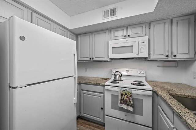 kitchen with white appliances, gray cabinetry, dark hardwood / wood-style floors, light stone countertops, and a textured ceiling