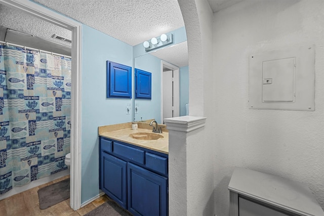 bathroom featuring electric panel, vanity, wood-type flooring, a textured ceiling, and toilet