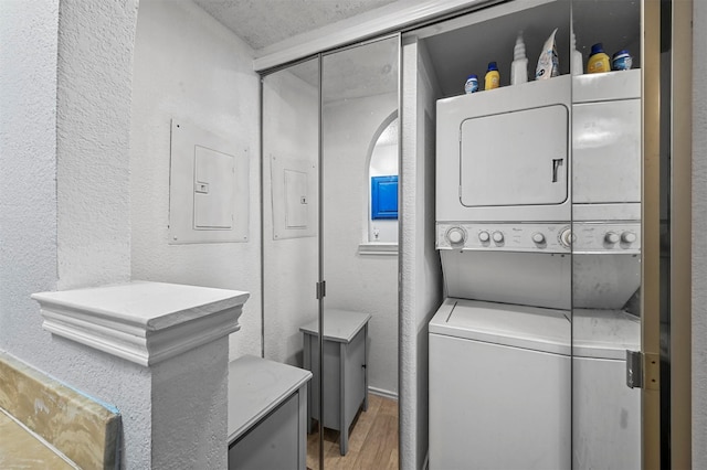 laundry room featuring stacked washing maching and dryer, wood-type flooring, and electric panel