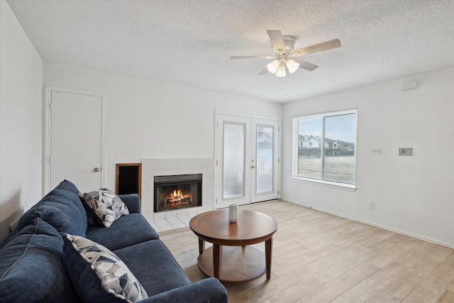 living area featuring baseboards, a tiled fireplace, light wood-style flooring, a textured ceiling, and a ceiling fan