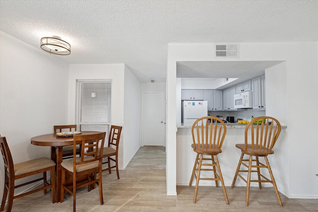 dining area featuring light wood finished floors, visible vents, a textured ceiling, and baseboards