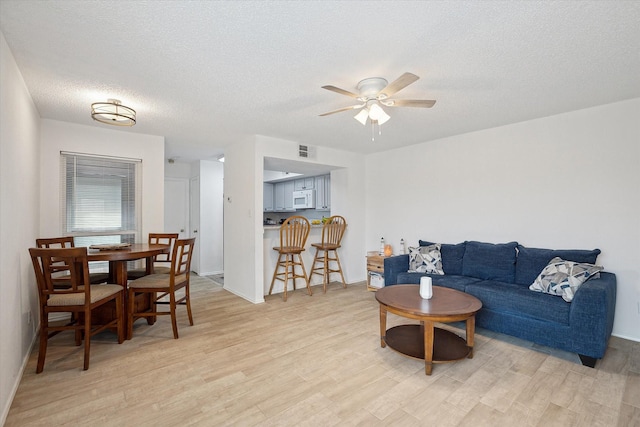 living area featuring visible vents, baseboards, ceiling fan, light wood-style floors, and a textured ceiling