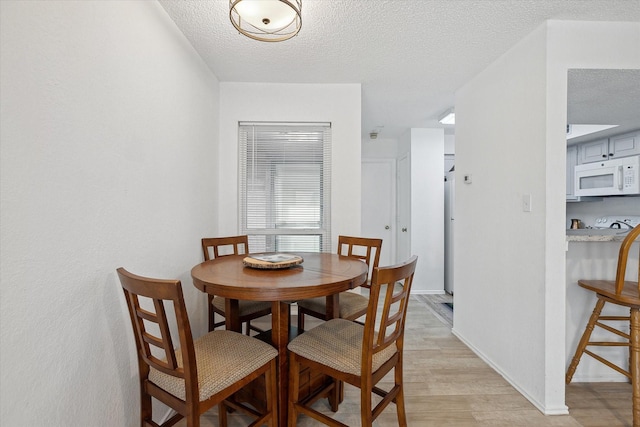 dining area with baseboards, light wood finished floors, and a textured ceiling