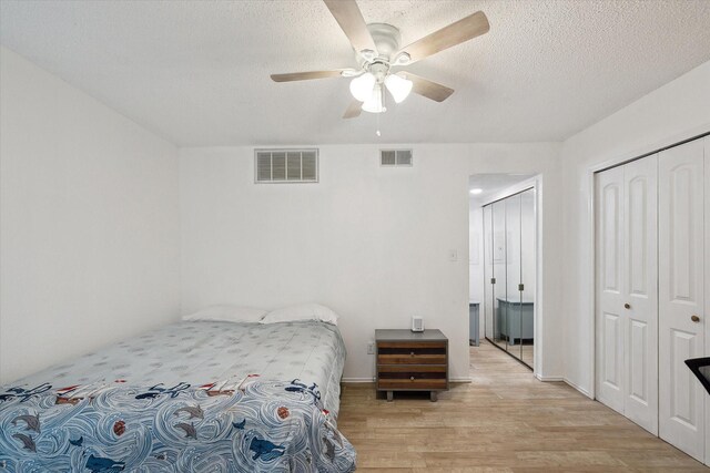 bedroom with light wood-type flooring, visible vents, a textured ceiling, and a closet