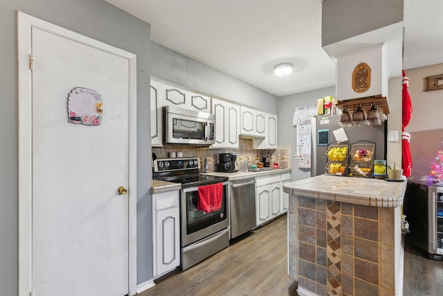 kitchen featuring stainless steel appliances, tasteful backsplash, light hardwood / wood-style flooring, tile countertops, and white cabinets