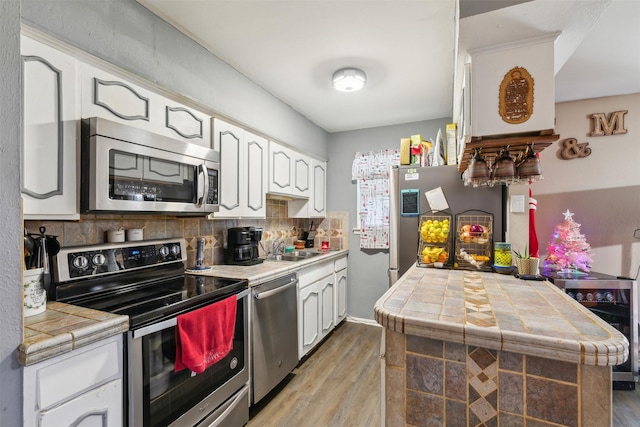 kitchen with backsplash, stainless steel appliances, sink, white cabinetry, and tile counters