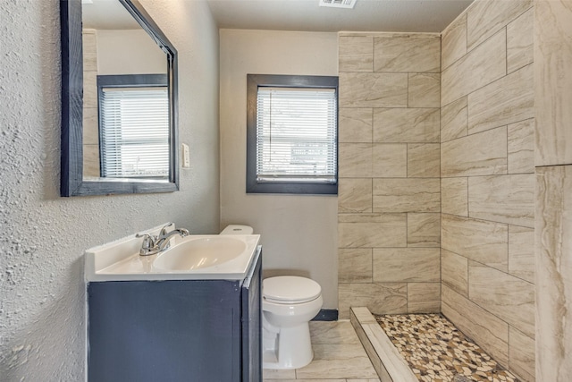 bathroom with tiled shower, tile patterned floors, vanity, and toilet