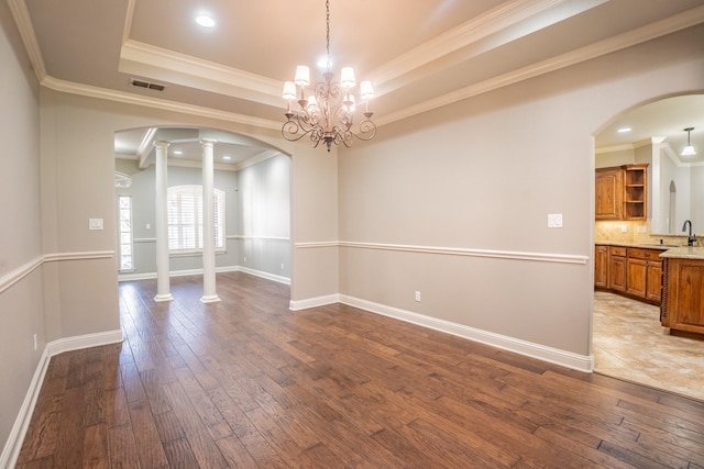 unfurnished dining area featuring decorative columns, crown molding, a chandelier, and hardwood / wood-style flooring