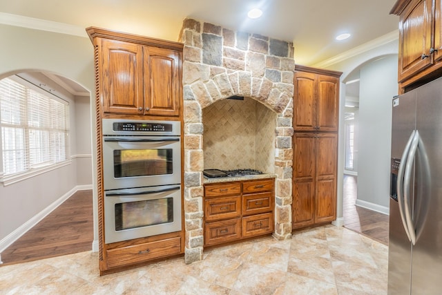 kitchen featuring appliances with stainless steel finishes, backsplash, light stone counters, crown molding, and light hardwood / wood-style floors