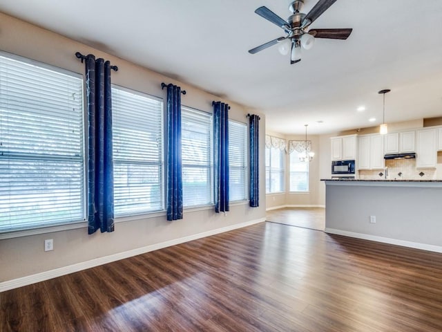 unfurnished living room with ceiling fan with notable chandelier and dark hardwood / wood-style floors