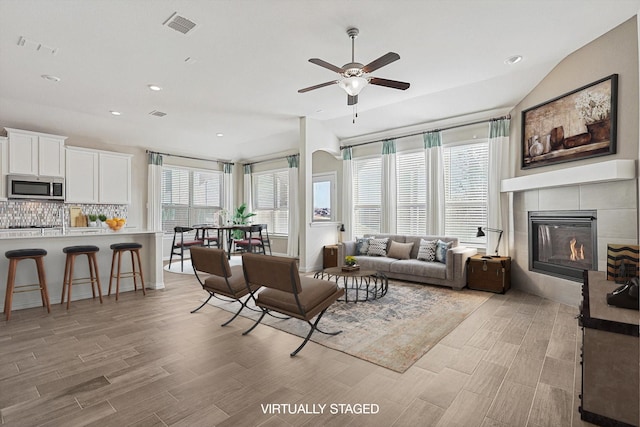 living room featuring a tile fireplace, light hardwood / wood-style floors, vaulted ceiling, and ceiling fan