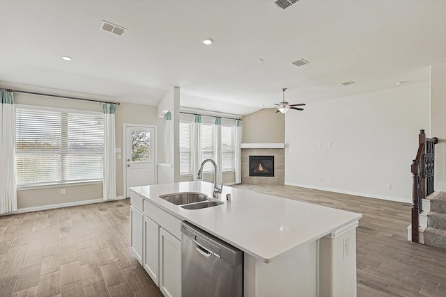 kitchen with sink, a tile fireplace, a center island with sink, dishwasher, and white cabinetry