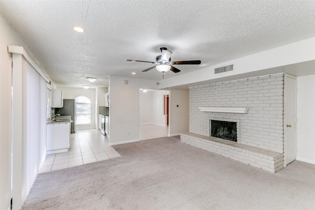 unfurnished living room featuring light carpet, ceiling fan, a textured ceiling, and a brick fireplace