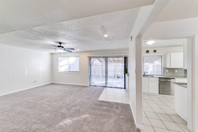 unfurnished living room with ceiling fan, sink, light colored carpet, and a textured ceiling