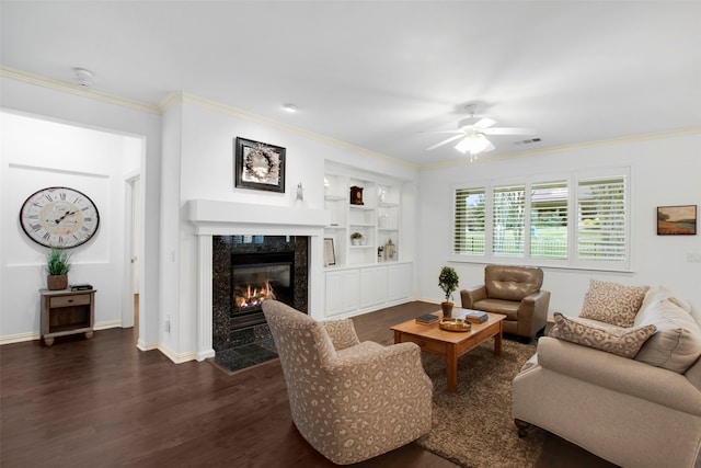 living room with dark hardwood / wood-style floors, ceiling fan, built in features, a fireplace, and ornamental molding