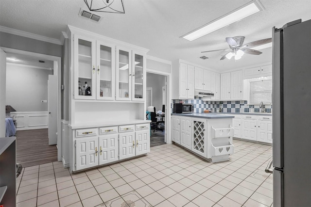 kitchen featuring white cabinets, ornamental molding, a textured ceiling, and stainless steel refrigerator