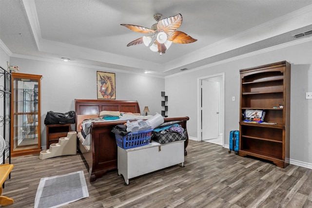 bedroom featuring ceiling fan, wood-type flooring, ornamental molding, and a tray ceiling