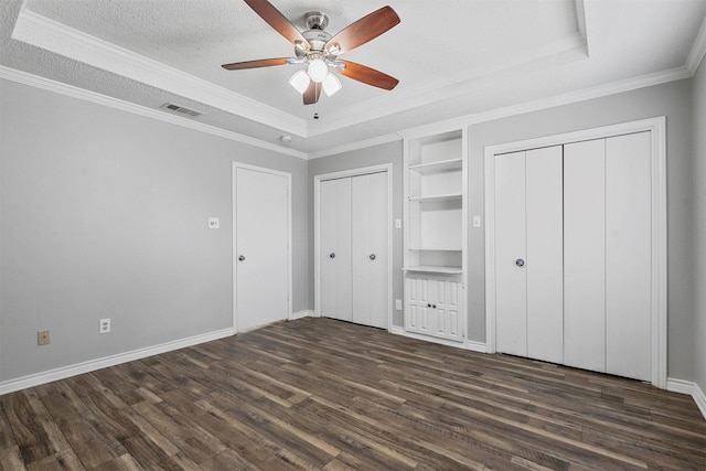 unfurnished bedroom with ceiling fan, a raised ceiling, dark hardwood / wood-style floors, a textured ceiling, and ornamental molding