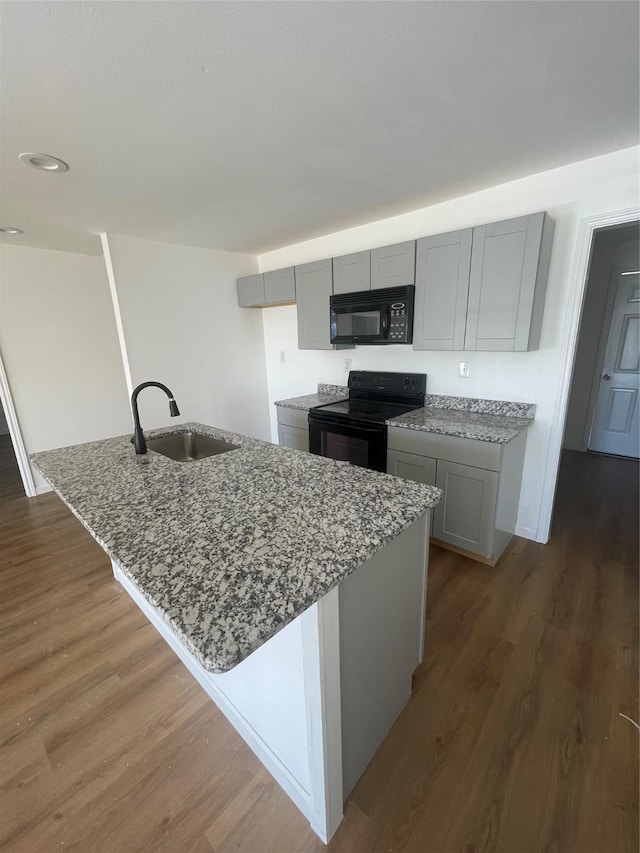 kitchen featuring black appliances, sink, gray cabinets, light stone countertops, and an island with sink