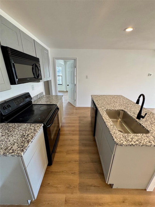 kitchen featuring black appliances, light stone counters, light wood finished floors, and a sink