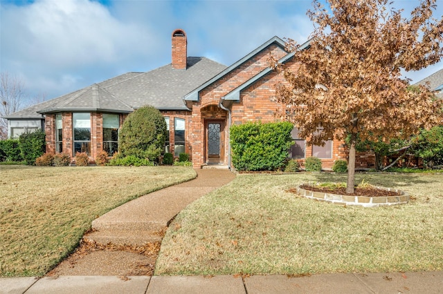 view of front of home featuring a shingled roof, a front yard, brick siding, and a chimney