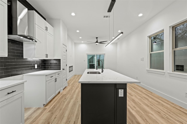 kitchen with white cabinetry, a kitchen island with sink, wall chimney exhaust hood, and sink