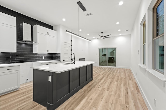 kitchen featuring pendant lighting, white cabinets, a center island with sink, wall chimney range hood, and ceiling fan