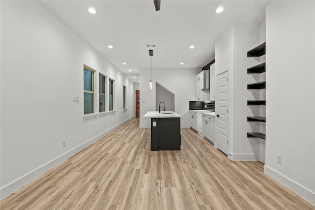 kitchen with light wood-type flooring, a kitchen island with sink, sink, decorative light fixtures, and white cabinetry