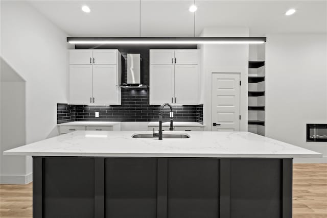 kitchen featuring white cabinets, a center island with sink, wall chimney exhaust hood, and sink