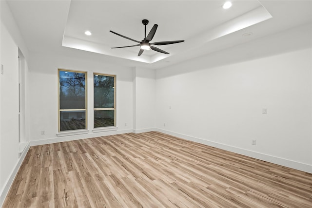 unfurnished room with ceiling fan, light hardwood / wood-style floors, and a tray ceiling