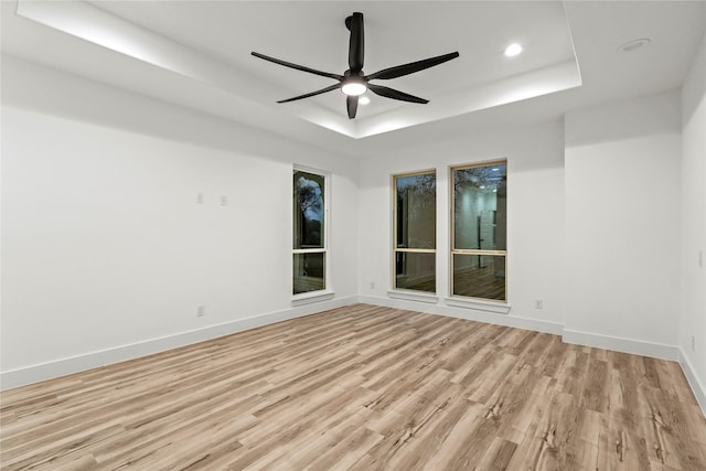 empty room featuring ceiling fan, light wood-type flooring, and a tray ceiling