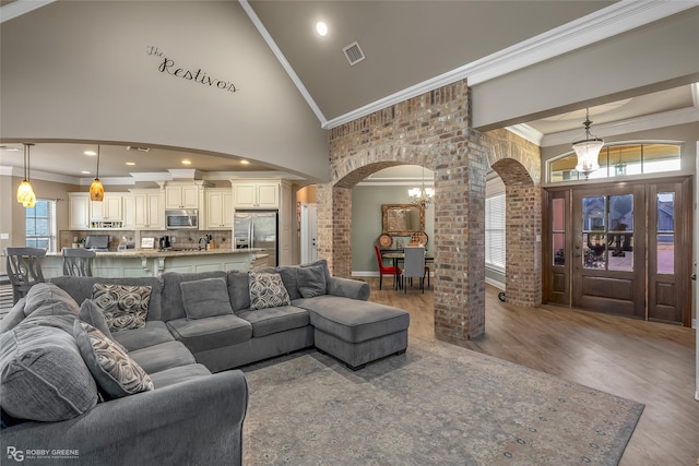 living room with hardwood / wood-style floors, crown molding, a chandelier, and high vaulted ceiling