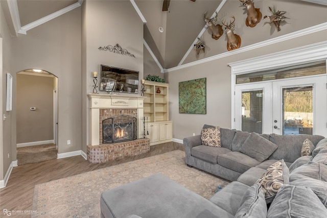 living room with a fireplace, high vaulted ceiling, hardwood / wood-style flooring, crown molding, and french doors