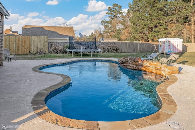 view of pool with a trampoline and a storage unit