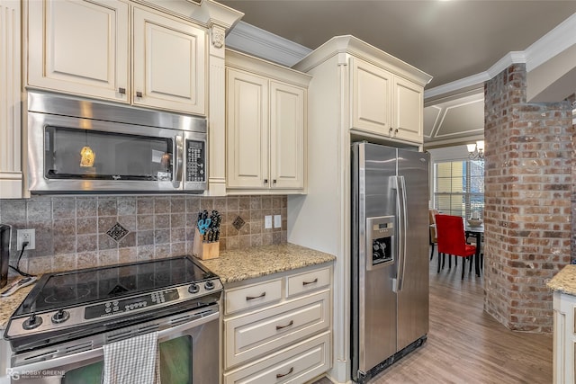 kitchen featuring ornamental molding, cream cabinetry, stainless steel appliances, light stone countertops, and backsplash