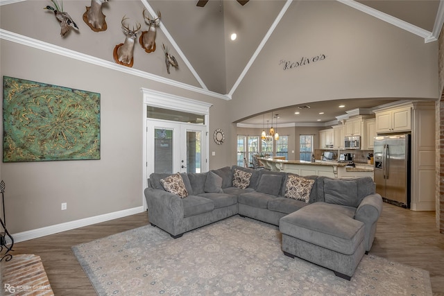 living room with crown molding, hardwood / wood-style floors, high vaulted ceiling, ceiling fan with notable chandelier, and french doors