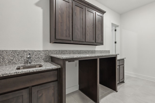 kitchen featuring dark brown cabinets, light stone counters, light tile patterned floors, and sink