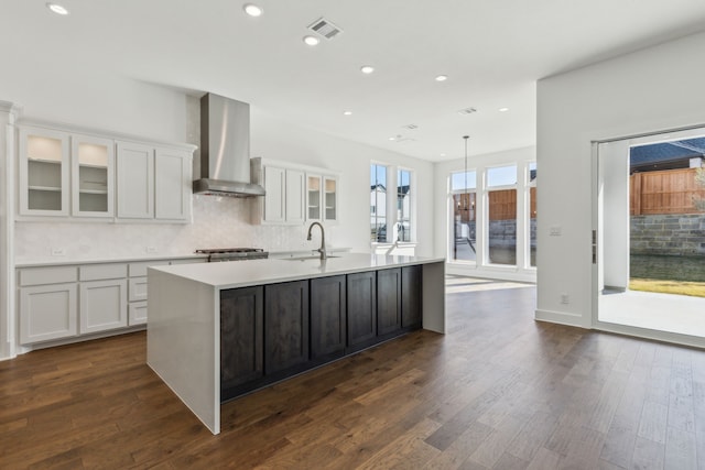 kitchen featuring a center island with sink, white cabinetry, dark wood-type flooring, and wall chimney range hood