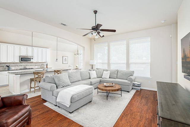 living room with dark hardwood / wood-style flooring, ceiling fan with notable chandelier, and sink