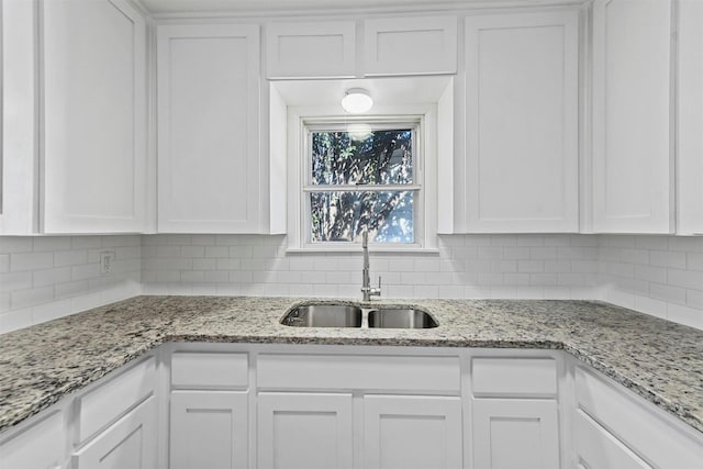 kitchen with white cabinetry, light stone countertops, and sink