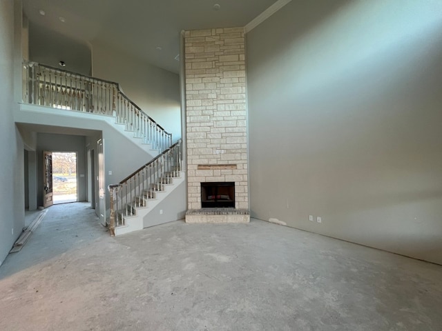 unfurnished living room with unfinished concrete floors, a fireplace, a towering ceiling, and stairs